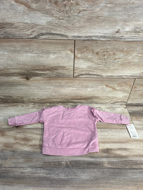 Flat lay of pink Cat & Jack baby sweatshirt (3–6 months) showing long sleeves and shoulder ruffle detail on wood background with tag attached