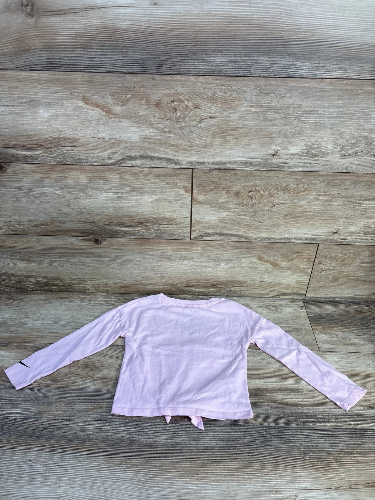 Back of pink Nike toddler long-sleeve shirt size 4T with tied hem and black swoosh on sleeve on wood background