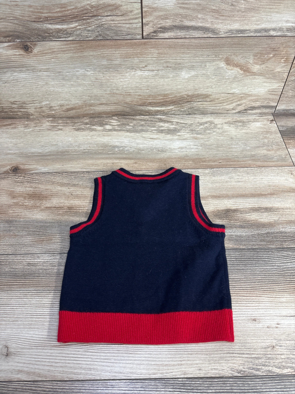 Navy blue and red sleeveless toddler sweater vest laid flat on wooden floor