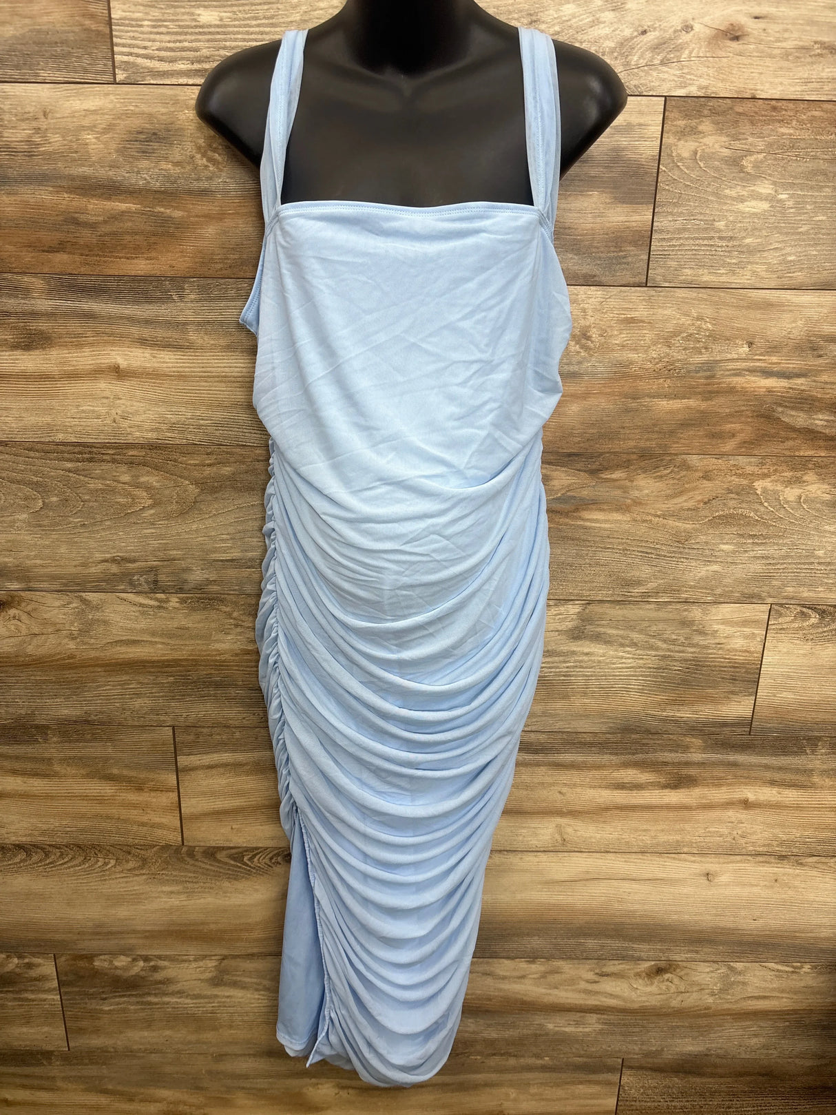 Light blue ruched maternity dress with thin straps, displayed on mannequin against wood flooring