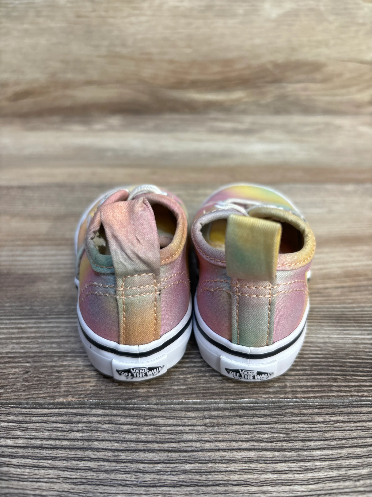 Back view of pastel tie-dye Vans toddler sneakers on wood background