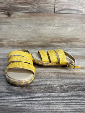 Three-quarter view of Janie and Jack Sunset Mood straw sandals in yellow showcasing woven straps and braided sole on wood plank floor