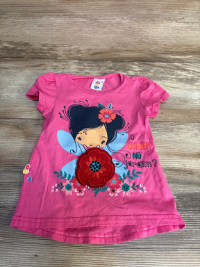 Pink kids t-shirt with fairy graphic, floral appliqué, and 'O que tem no jardim?' text, laid on wood floor