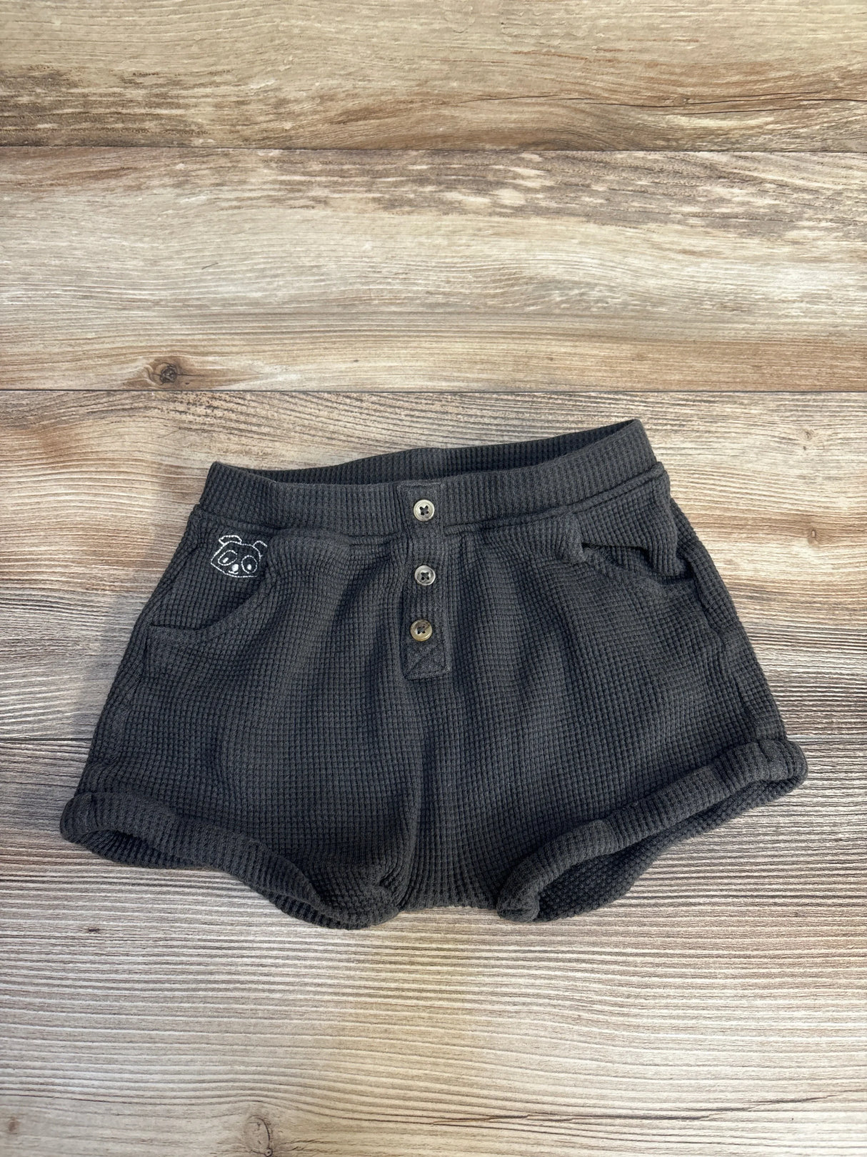 Dark gray baby shorts with panda embroidery, button front, ribbed cuffs on wood floor