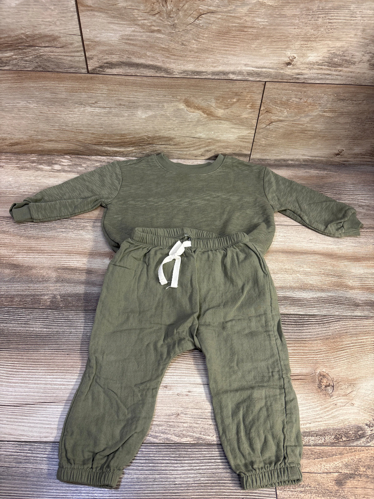 Top-down view of green two-piece sweatshirt and joggers set with elastic cuffs and white drawstring on wood-look flooring
