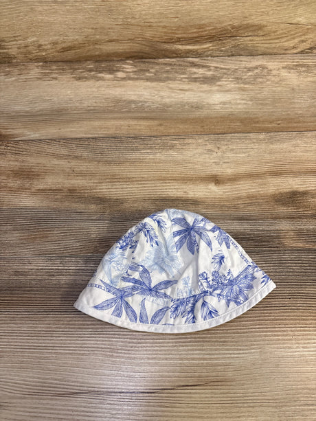 Top-down view of baby bucket hat showcasing blue palm tree print on white cotton, size 0-3 months, on light wood background