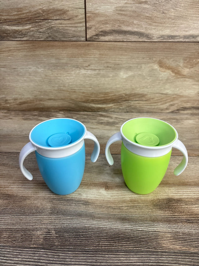 Front view of two Munchkin Miracle 360 trainer cups (blue and green) showing handles and spill-proof 360 rim on wood surface