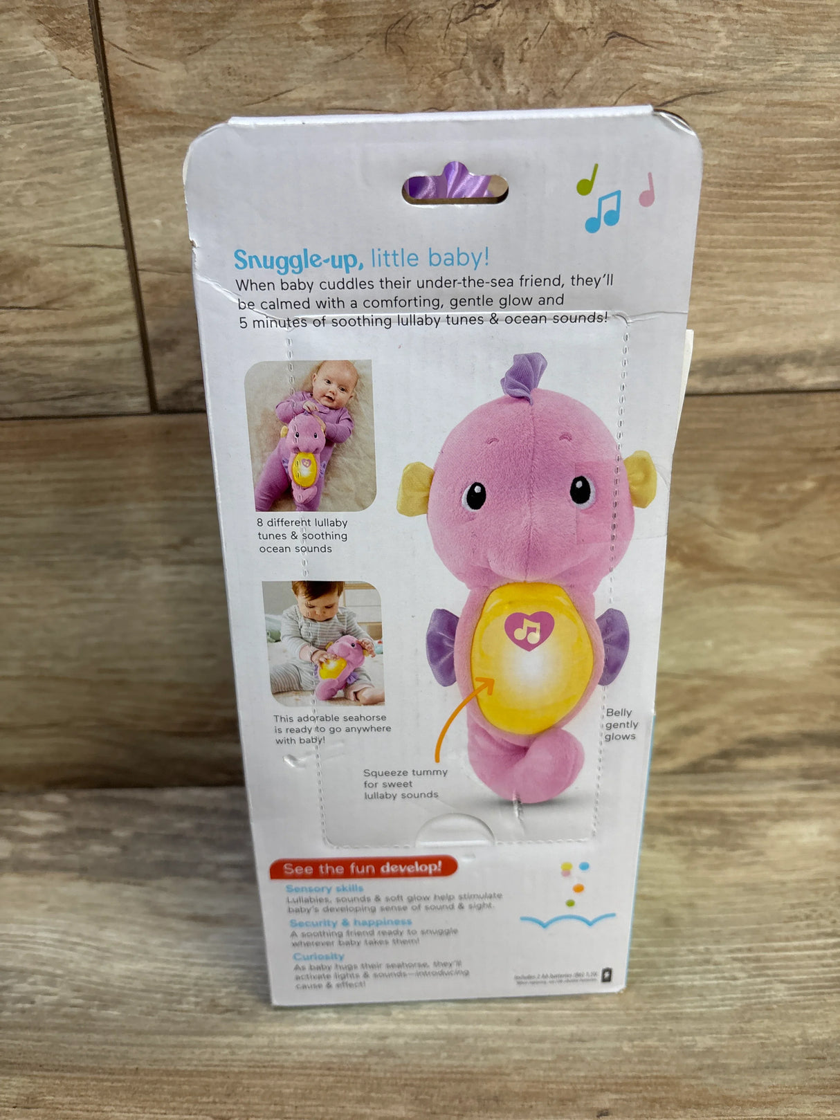 Front of boxed Soothe & Glow Seahorse (Fisher-Price) pink showing glowing yellow belly on wooden surface