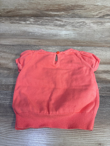 Flat-lay of coral short-sleeve knit sweater showing back keyhole button, puff sleeves and ribbed hem on light wood