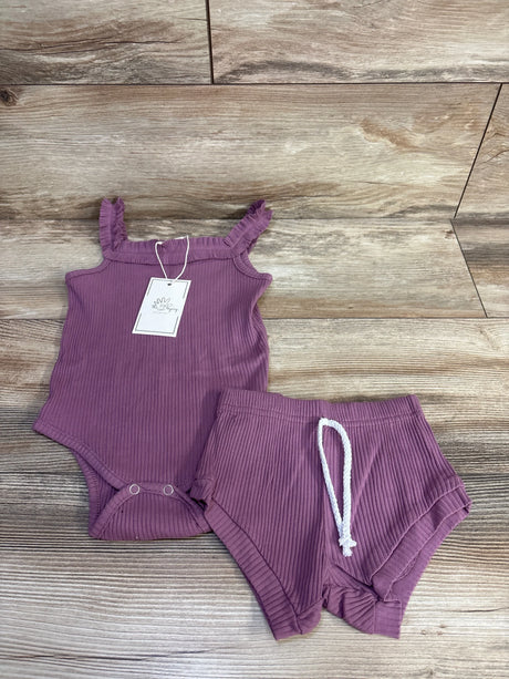 Flat lay of purple ribbed 2-piece tank bodysuit and bottoms showing ruffled straps and snap crotch on wood background