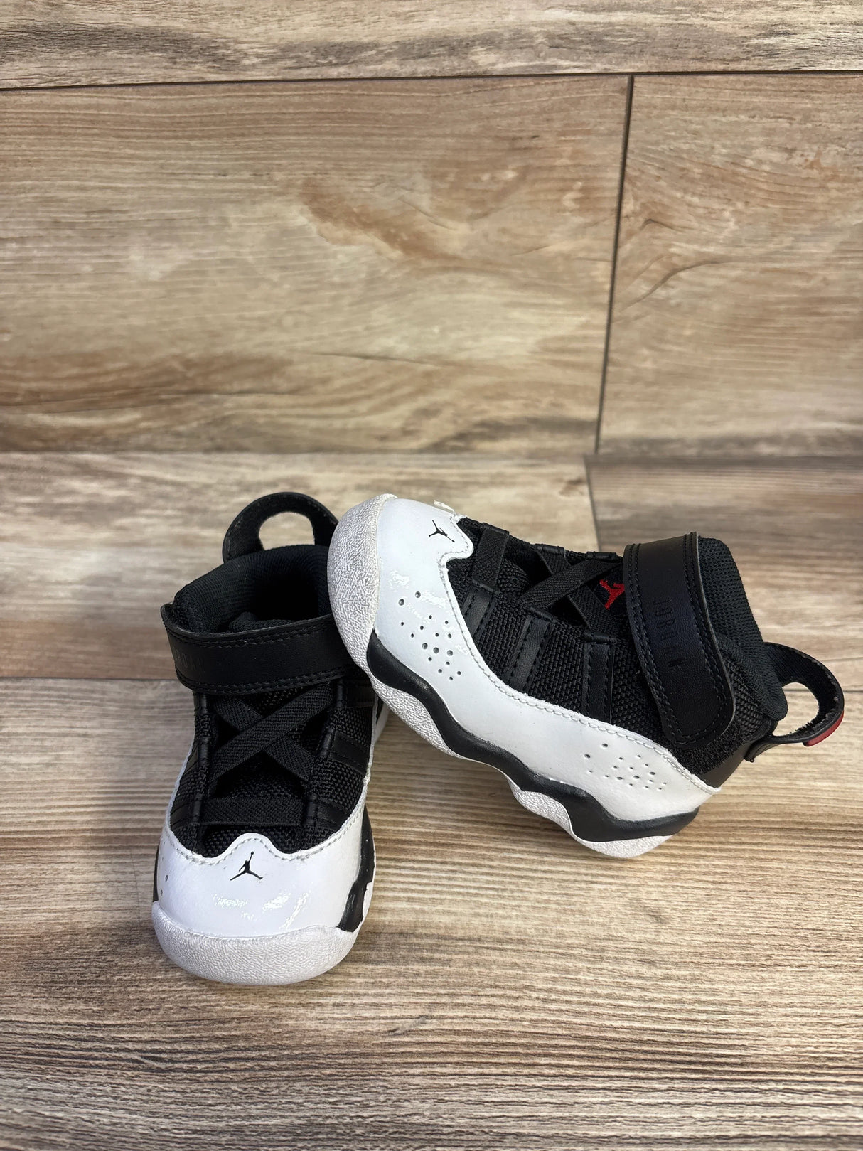 Angled front view of toddler Air Jordan 6 Rings sneakers in black/white/red showing Velcro strap and Jumpman logo on wood