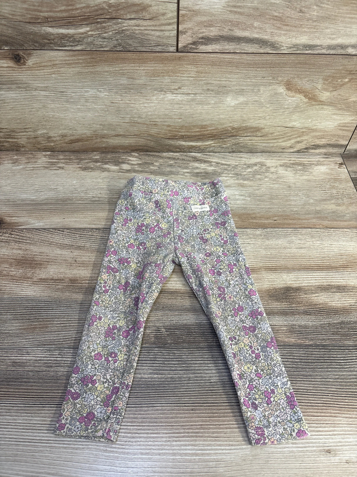 Flat lay front view of cream Zara ribbed leggings 18m showing small pink, purple and yellow floral print on wood background