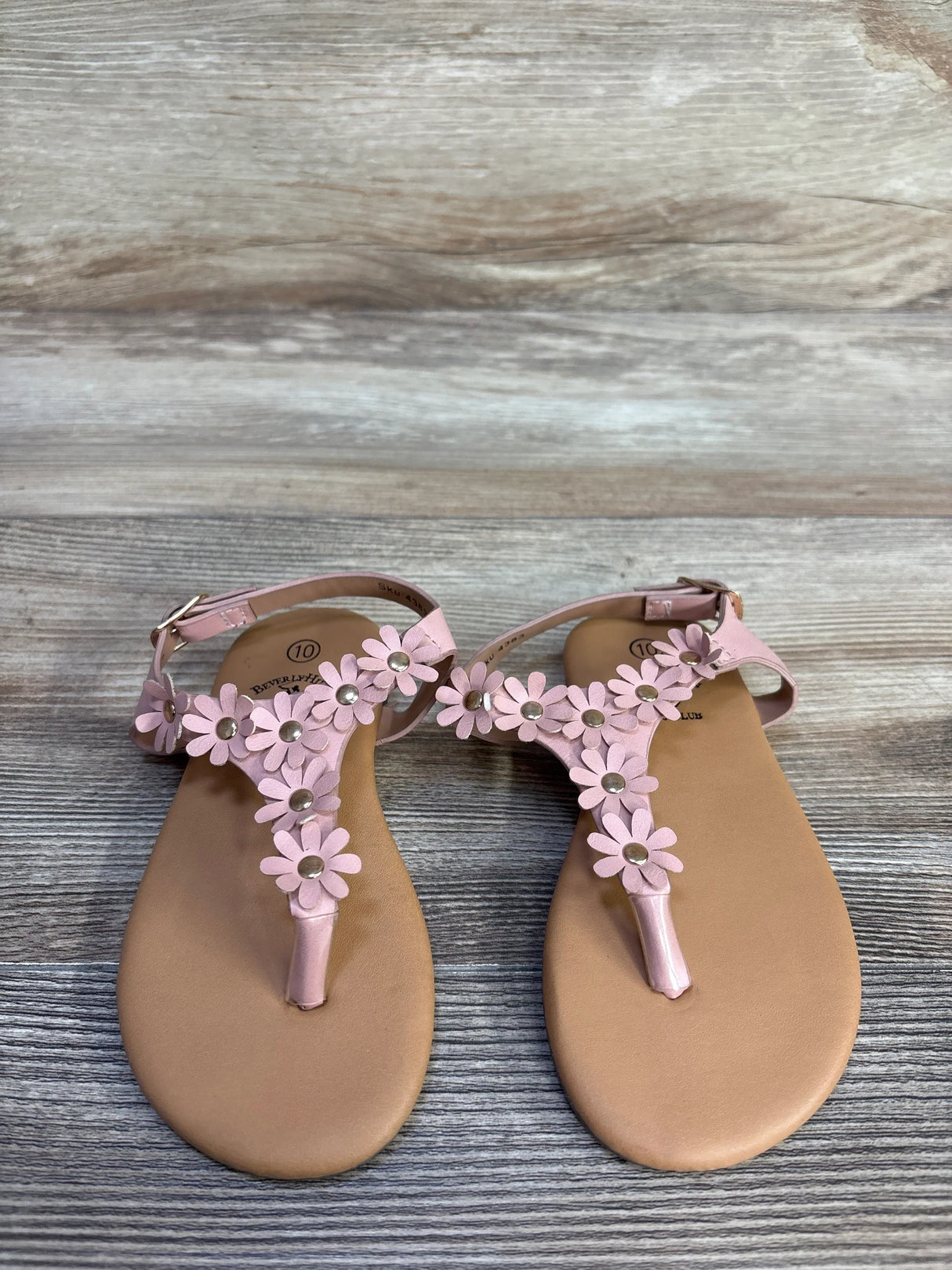 Top down view of pink toddler T strap sandals showcasing daisy floral straps with gold studs on wood plank background
