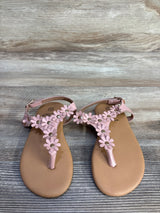 Top down view of pink toddler T strap sandals showcasing daisy floral straps with gold studs on wood plank background