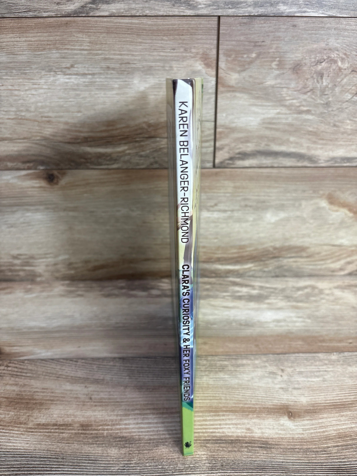 Spine of a children's book titled Clara's Curiosity & Her Foxy Friends by Karen Belanger-Richmond on wooden surface