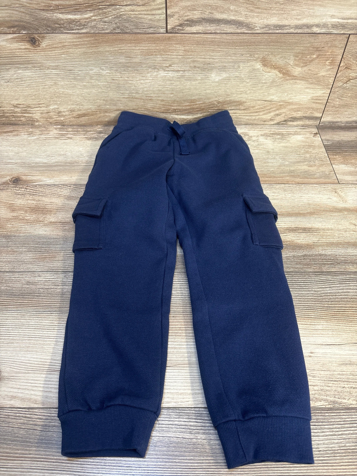 Navy blue kids cargo joggers with drawstring waist, laid flat on wood floor