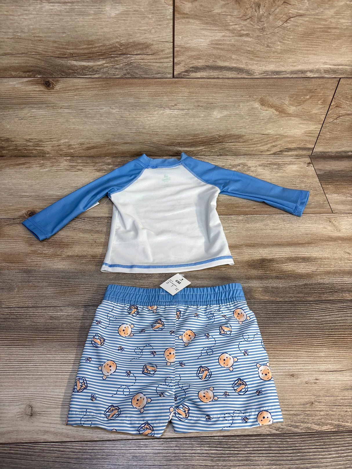 Blue and white baby swim set with Winnie the Pooh print, size 6M, laid on wood floor