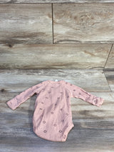 Flat lay of pink Kate Quinn organic kimono newborn bodysuit showcasing long sleeves and small floral eyelet pattern on wood plank background