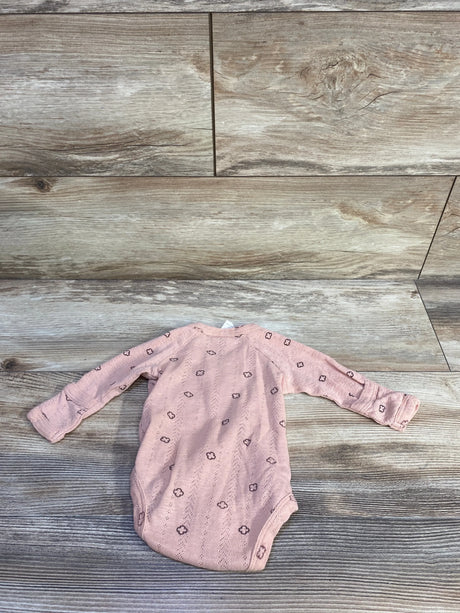 Flat lay of pink Kate Quinn organic kimono newborn bodysuit showcasing long sleeves and small floral eyelet pattern on wood plank background