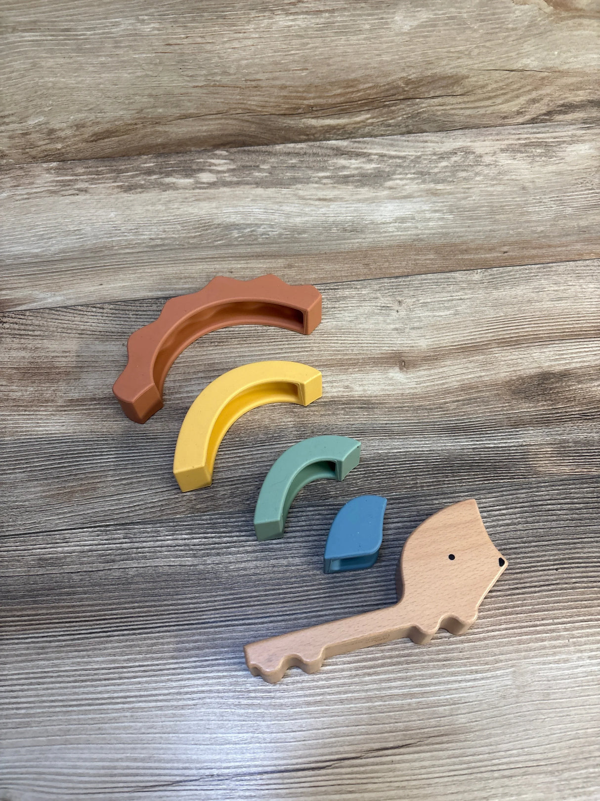 Top-down view of Cloud Island Silicone & Wood Hedgehog Stacker showing four colorful silicone arches and wooden hedgehog base on wood surface