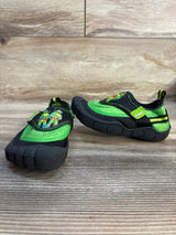 Kids' black and green slip-on shoes with cartoon turtle graphic, indoor wood background.