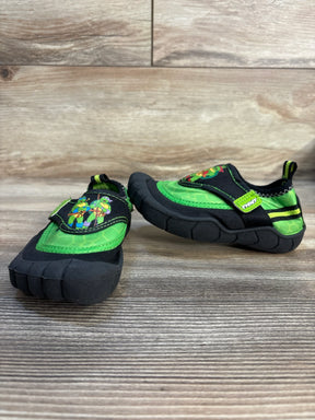 Kids' black and green slip-on shoes with cartoon turtle graphic, indoor wood background.