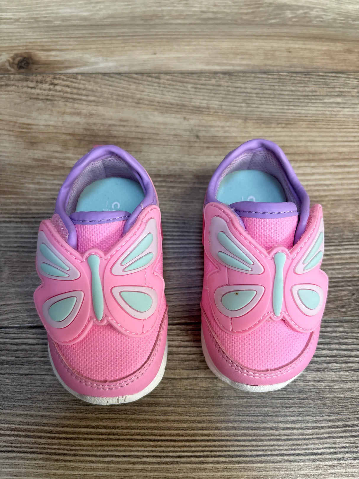 Pink toddler sneakers with butterfly wings on wooden floor