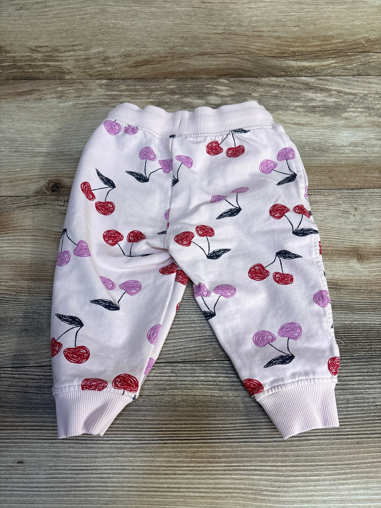Baby pink jogger pants with red and purple cherry print, displayed on wood surface