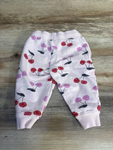 Baby pink jogger pants with red and purple cherry print, displayed on wood surface