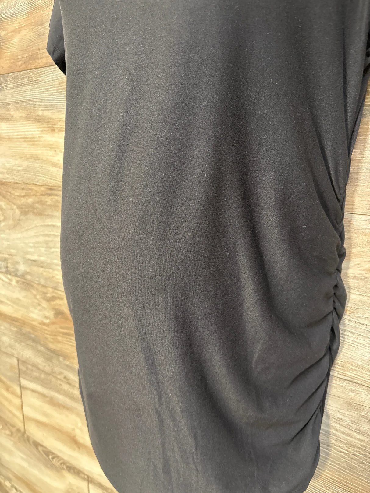 Close-up side view of Time and Tru maternity shirt showcasing ruched side seam and stretch black knit with wood plank background