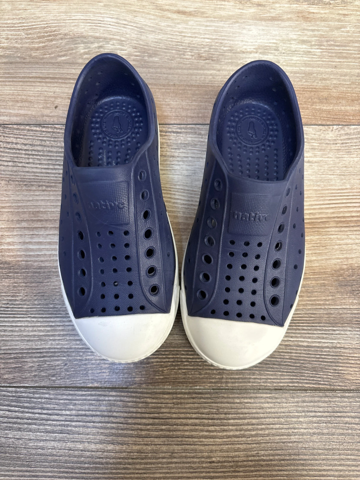 Navy blue slip-on kids shoes with white rubber toes and ventilation holes on wood floor