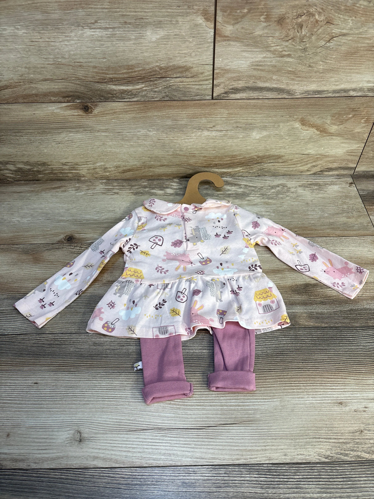 Pink baby outfit with printed long-sleeve top and matching leggings on wood background
