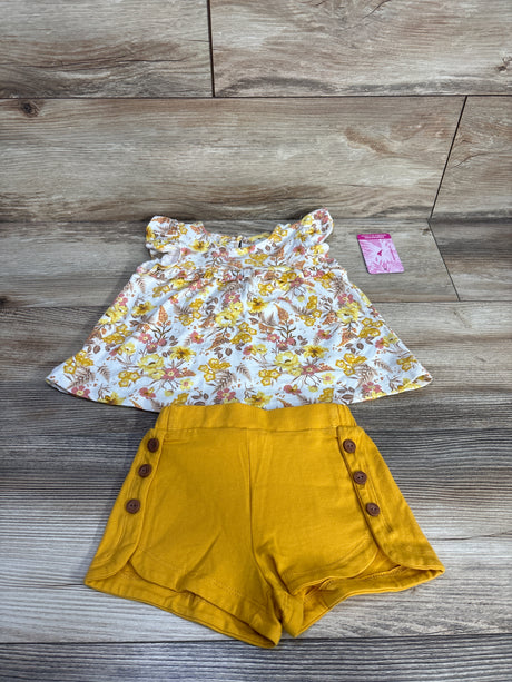 Flat lay of 2-piece baby floral flutter-sleeve top and mustard shorts, size 12 months, side button detail on wood background