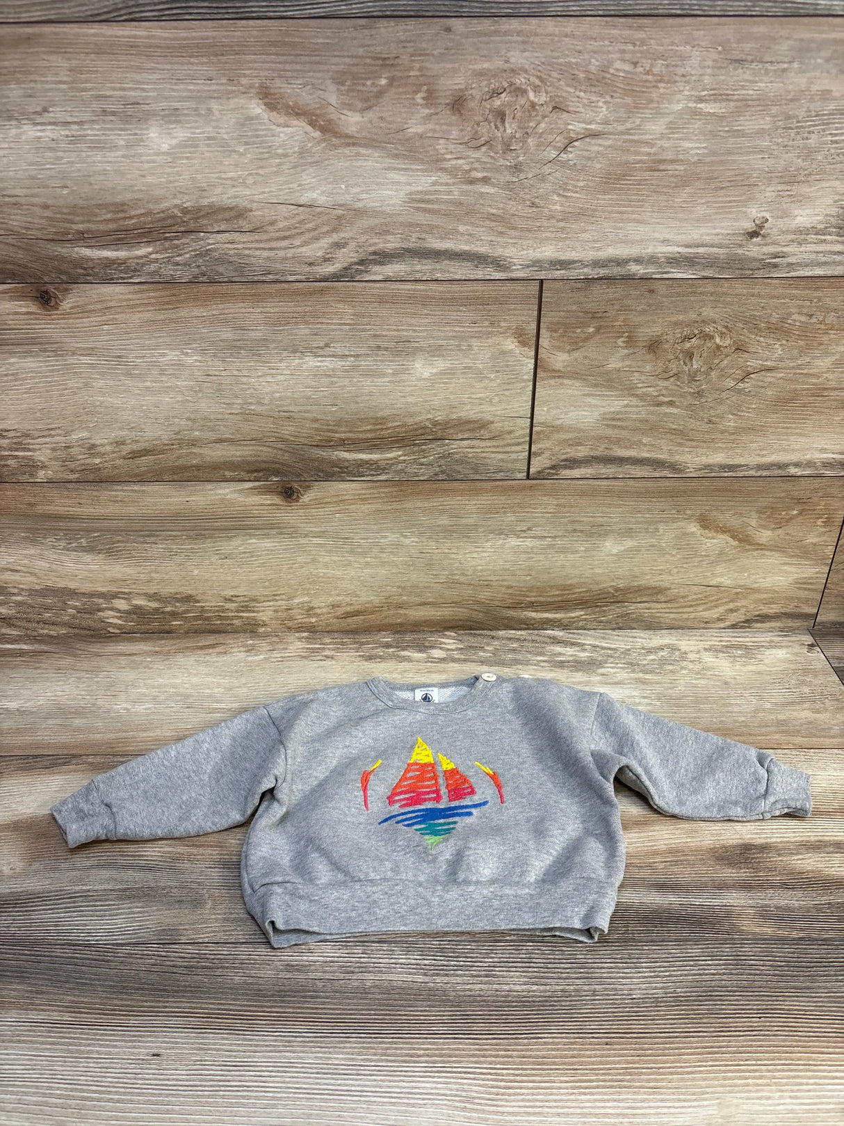 Gray kids sweatshirt with colorful sailboat graphic, laid flat on wood background