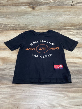 Flat lay black 4T T-shirt with 'Super Bowl LVII' and 'Las Vegas', central LVII logo and red patch on wood background