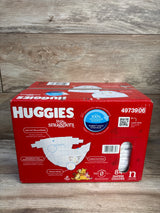 Front view of Huggies Little Snugglers newborn diaper box, 84 count, showing diaper illustration, wetness indicator labels and side window on wood background