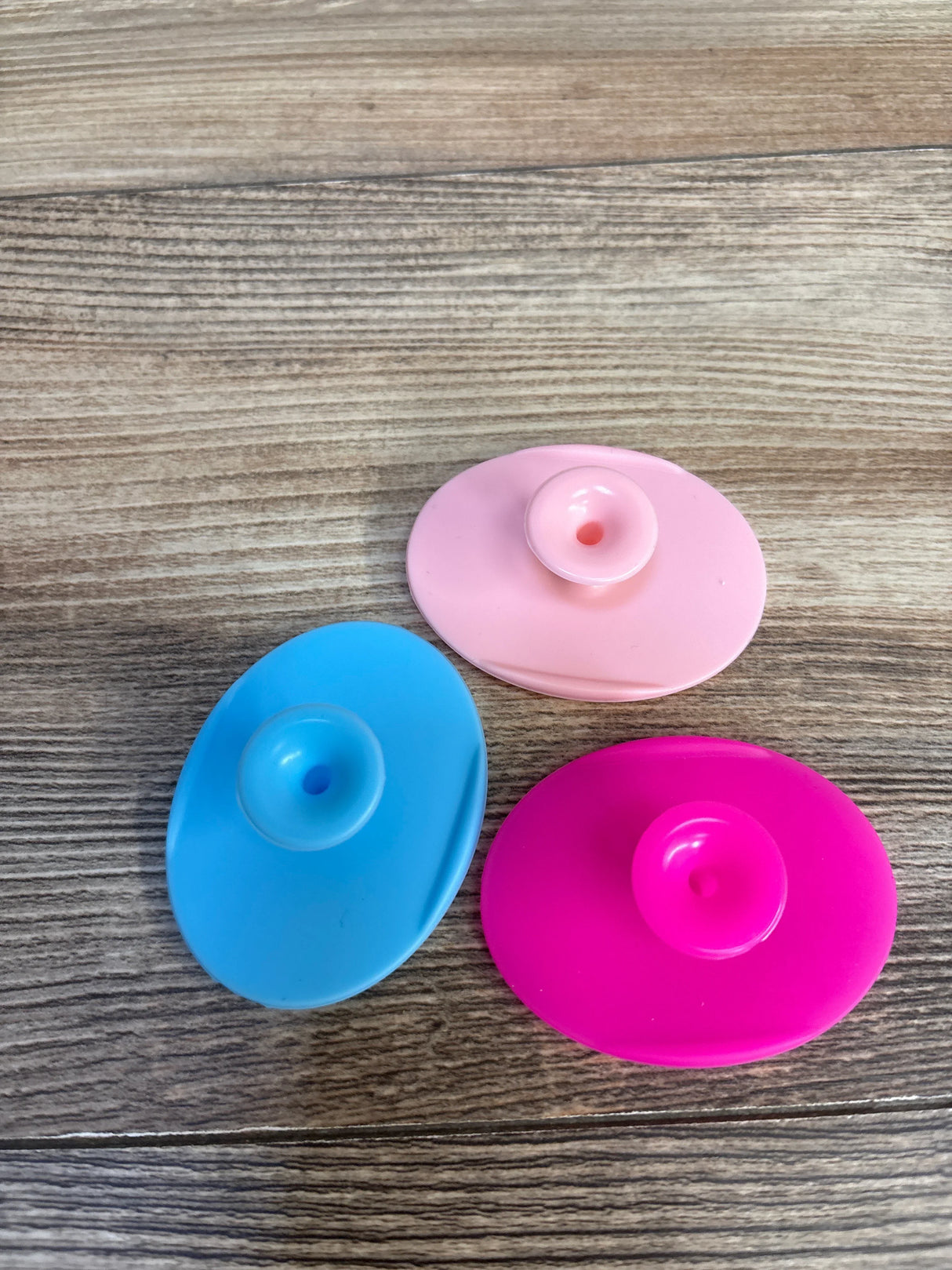 Three colorful baby bath toys in blue, pink, and magenta on wood surface