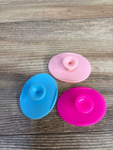 Three colorful baby bath toys in blue, pink, and magenta on wood surface