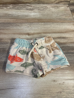 Top-down view of Carter's beige baby shorts with multicolored fish print and drawstring waistband on wood plank background
