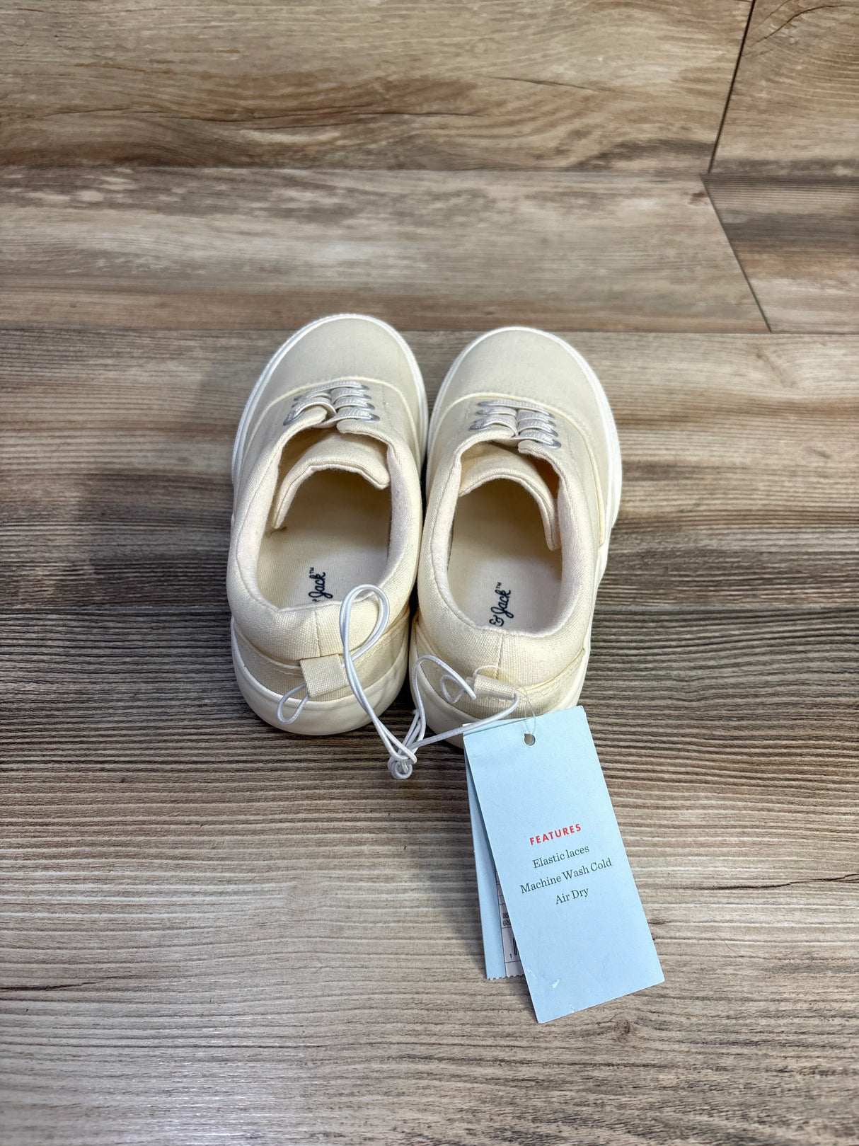 Top view of Cat & Jack toddler slip-on sneakers, off-white size 13C, showing elastic laces and tag on wood background