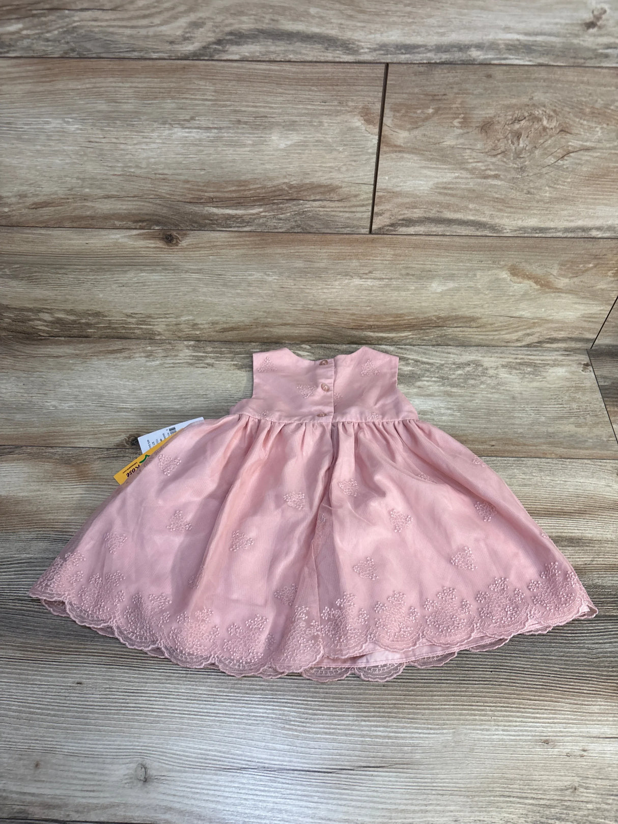 Pink baby dress with floral embroidery and lace hem, laid on wood floor