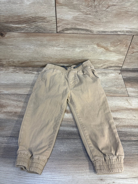 Beige kids jogger pants with elastic waist and cuffs, laid on wood floor