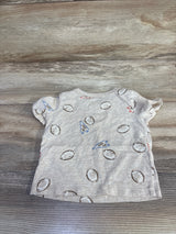Front view of beige First Impressions baby football-print shirt showcasing short ruffle sleeves and all-over football and pennant print on wood background