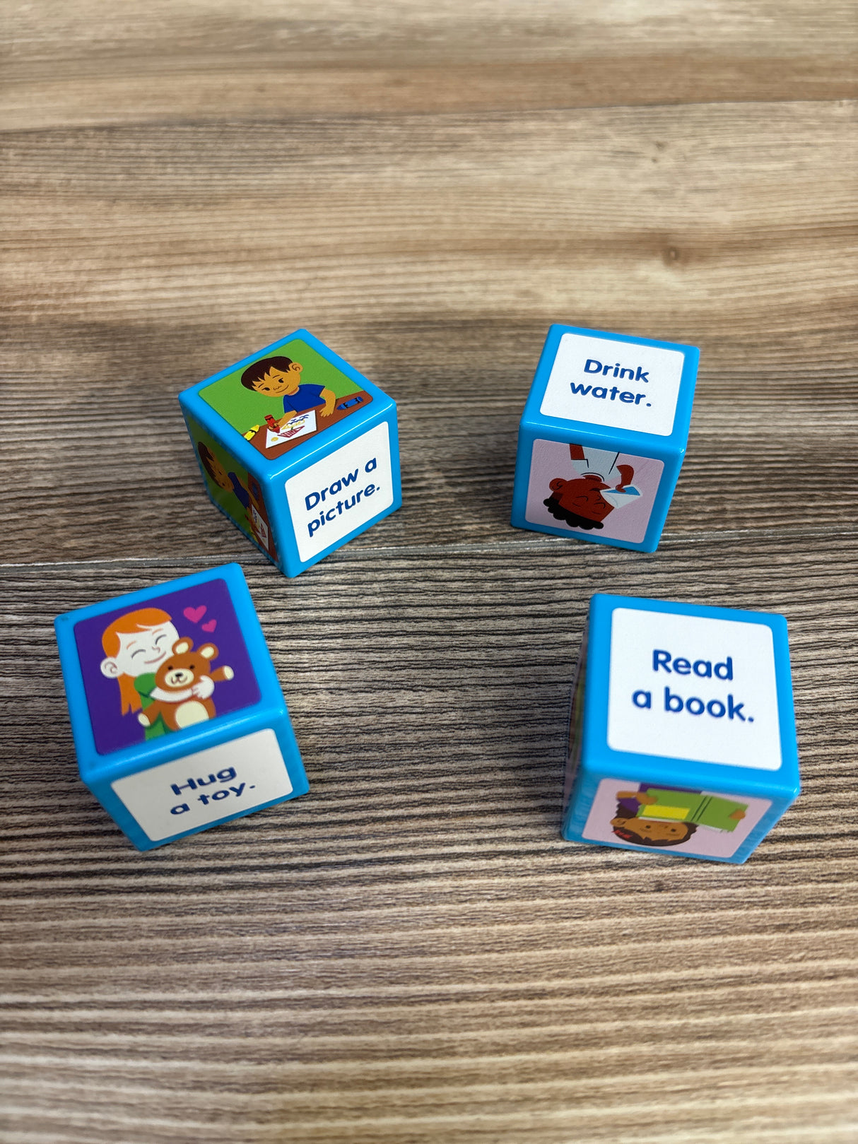 Angled view of Lakeshore Calm Down Cubes with prompts Draw a picture, Drink water, Hug a toy, Read a book on wood tabletop