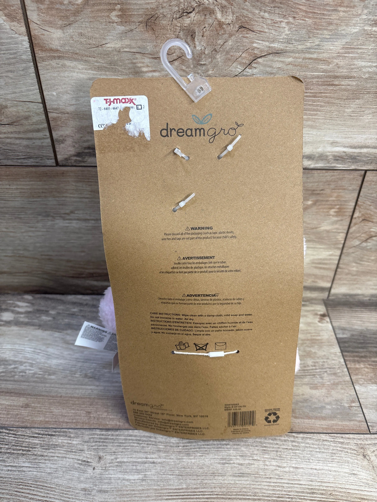 Back of DreamGro Lullaby Travel Soother packaging showing clear stroller hook and pink elephant plush with wood floor background