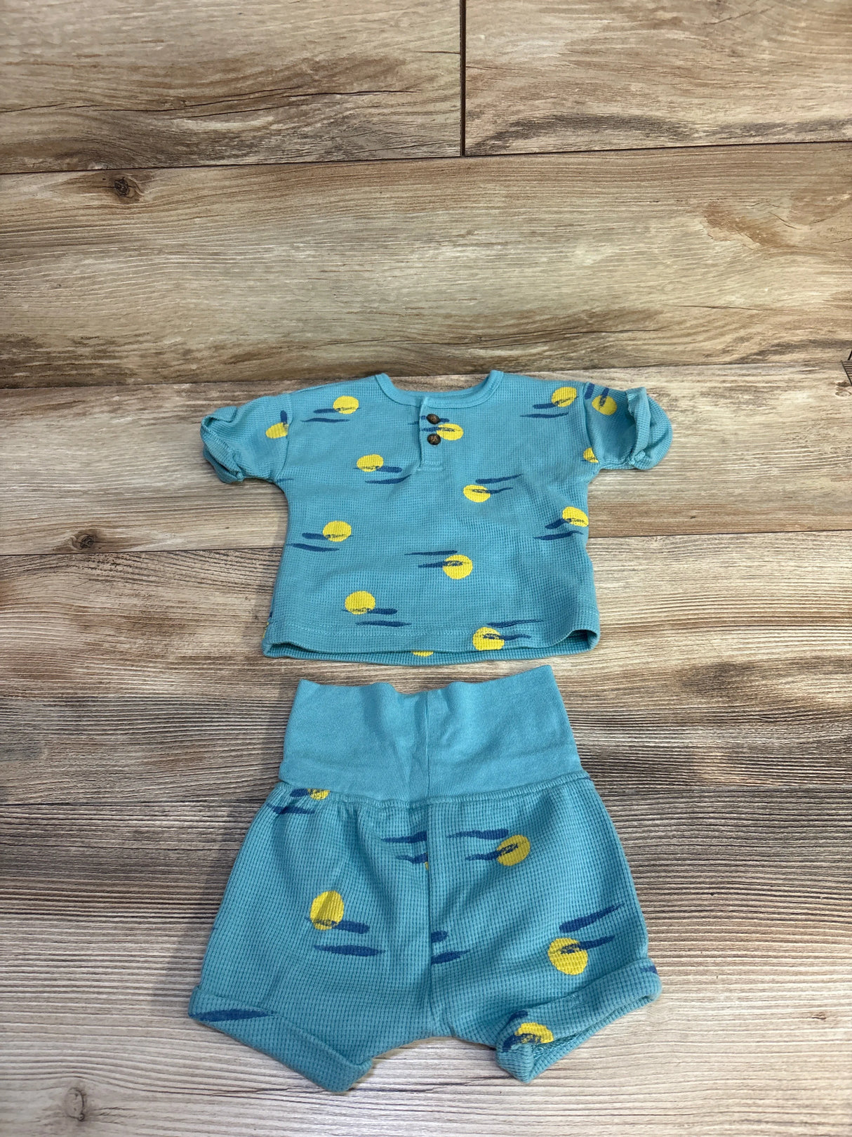 Flat lay of teal waffle-knit henley shirt and matching shorts with yellow circle print, size 0-3 months on wood background