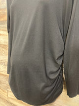 Close-up back view of Ekouaer black ruched long-sleeve maternity top showing side ruching on wood-panel background