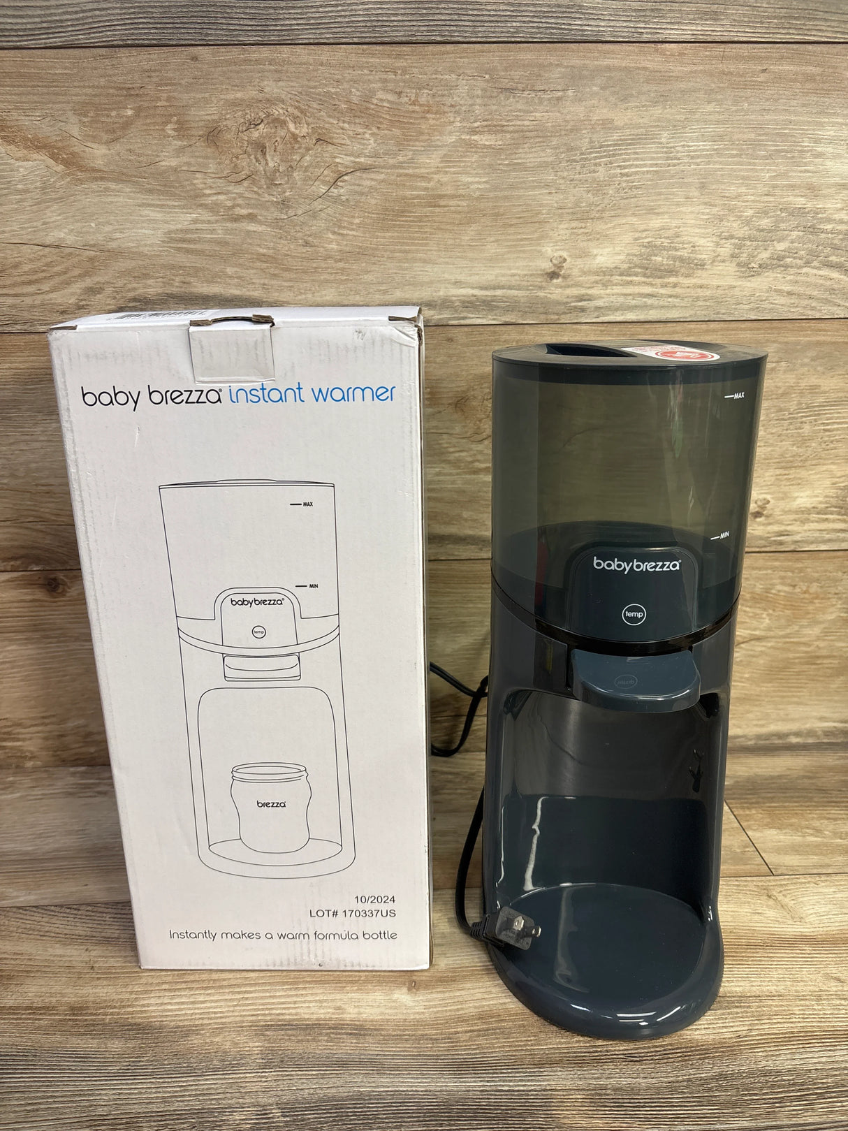 Front view of Baby Brezza Instant Bottle Warmer in black showcasing clear water reservoir and front dispensing tray with wood background