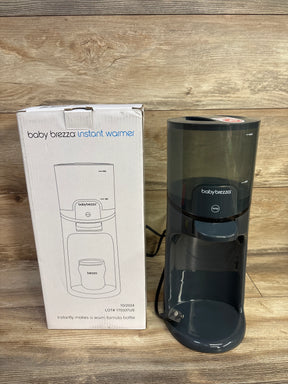 Front view of Baby Brezza Instant Bottle Warmer in black showcasing clear water reservoir and front dispensing tray with wood background