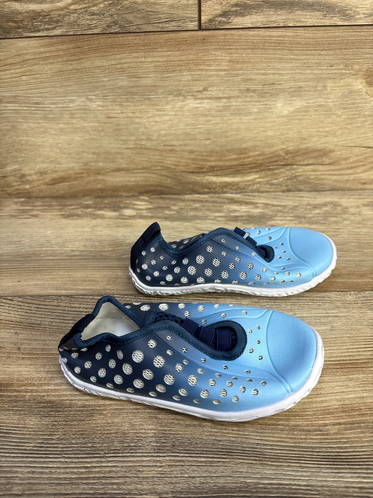 Top-down view of children's Fires Barefoot blue quick-dry water shoes showing perforated breathable upper and white sole on wooden floor